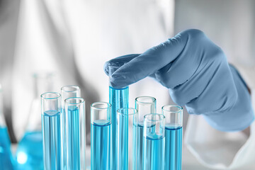 Scientist taking test tube with light blue liquid in laboratory, closeup