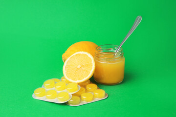 Cough drops, fresh lemons and honey on green background