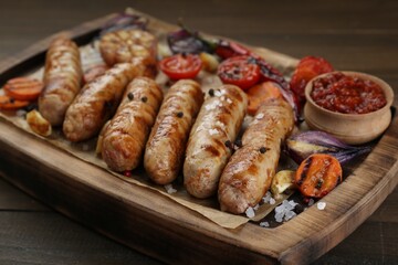 Tasty grilled sausages with vegetables on wooden table, closeup