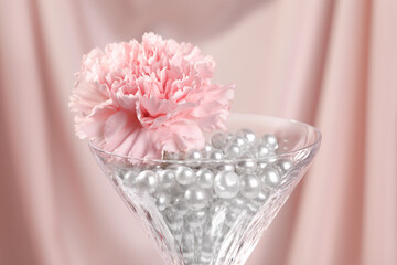 Martini glass with silver beads and pink flower near cloth, closeup
