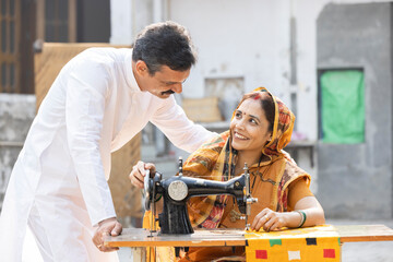 Indian rural woman using sewing machine and her husband.