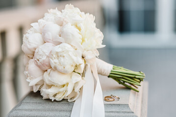 Wedding rings bride and groom with bridal bouquet flowers white peonies. Two beautiful golden...