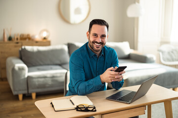 Portrait of a smiling man, working over the laptop, holding phone, and sitting at the office.