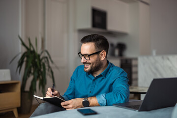 Businessman writing notes in the notebook, sitting on the floor at the workplace.