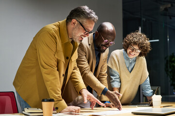 Group of three intercultural brokers in smart casualwear discussing document with financial data...