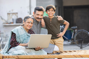 Rural Indian parents with son using laptop at village
