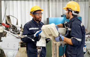 Multiracial engineer uses remote control board to check robotic welder operation in modern...