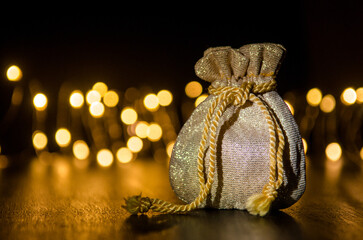 Small golden gift bag on black background illuminated by light from side, round yellow blurred lights behind