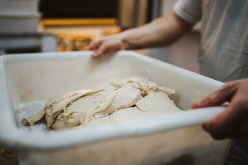 Baker man holding plastic tray with uncooked fresh bread dough in it