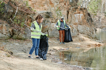Young people cleaning lakeshore, using special tools for picking up garbage
