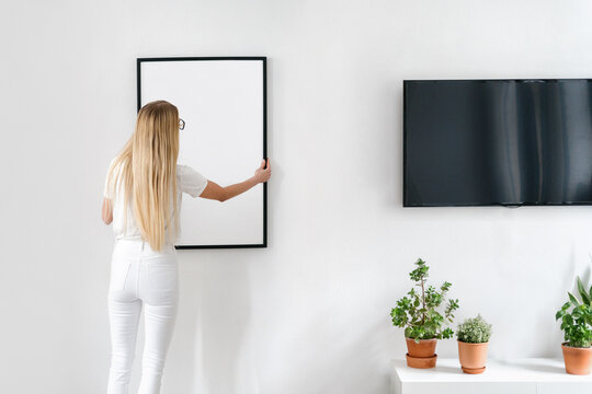 Woman Hanging Picture On Wall In Room