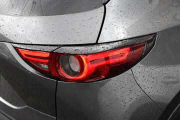 Car with switched on tail light in drops of water, closeup