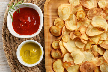 Tasty homemade parsnip chips with different sauces on wooden table, flat lay