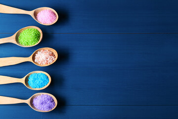 Spoons with colorful sea salt on blue wooden table, flat lay. Space for text