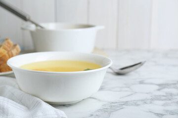 Fototapeta na wymiar Delicious bouillon in bowl on white marble table, closeup