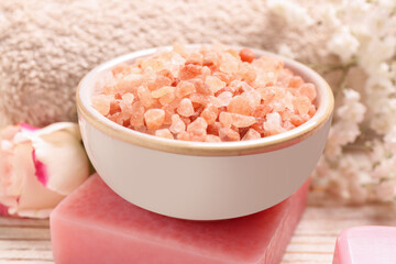 Bowl with sea salt and soap bar on white wooden table, closeup