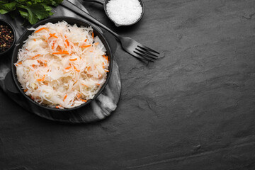 Bowl of tasty sauerkraut and ingredients on black table, flat lay. Space for text