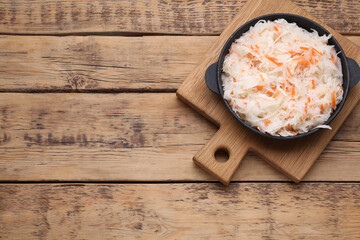 Bowl of tasty sauerkraut on wooden table, top view. Space for text