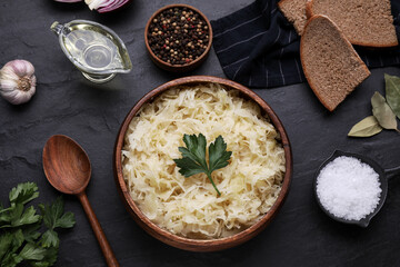 Bowl of tasty sauerkraut and ingredients on black table, flat lay