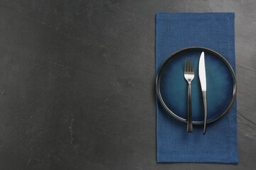 Ceramic plate, fork and knife on black table, top view. Space for text