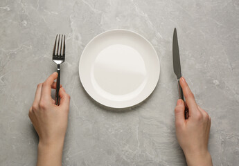 Woman with empty plate and cutlery at light grey table, top view