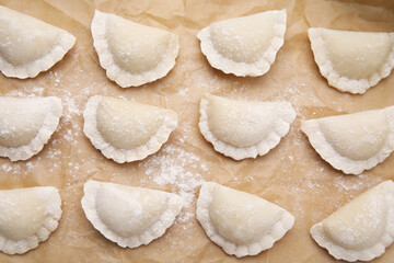 Fototapeta na wymiar Raw dumplings (varenyky) with tasty filling and flour on parchment paper, flat lay
