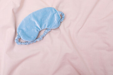 Light blue sleep mask on beige cloth, top view. Space for text