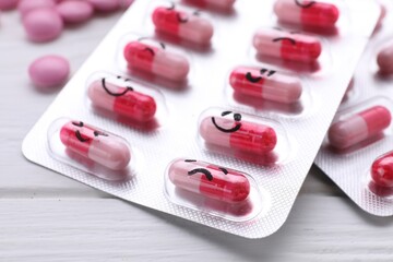 Blister of antidepressants with different emoticons on white wooden table, closeup
