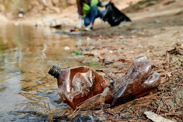 Plastic bottle on dirty beach of forest lake, Earth day concept