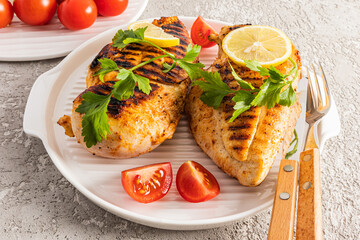 two grilled chicken breasts on a white serving tray with parsley, lemon, tomato slices. close-up. diet food.