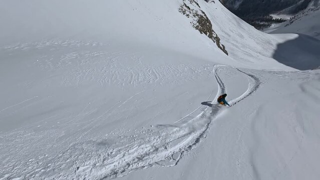 Male snowboard extreme heliski freeride from mountain fresh snow summit with avalanche backpack aerial view. FPV sport drone follow shot man snowboarding speed riding trick maneuver on crag slope 4k