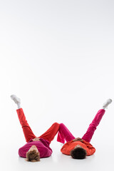 interracial couple in magenta color clothes lying on floor and showing w letter with legs on white background.