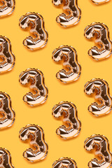 Repetitive pattern made of number 3 golden balloons. Creative layout on a yellow background.