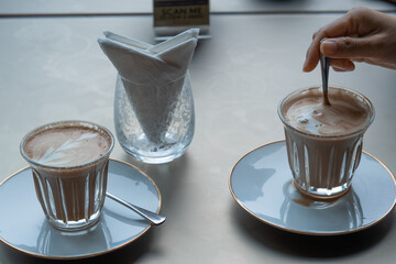 Capaccino in glass with hand stirring, Side view of coffee cup on the table.