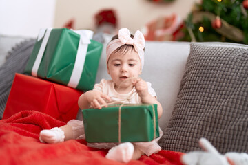 Obraz na płótnie Canvas Adorable toddler opening christmas gift sitting on sofa at home