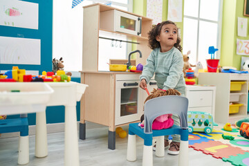 Adorable hispanic girl playing with play kitchen standing at kindergarten