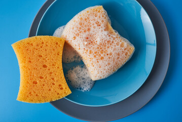 Yellow soapy sponge with foam on blue plate. Cleaning concept. Copy space
