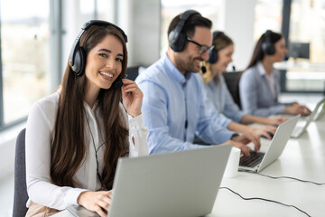 Beautiful friendly online support agent with headset working in row with her colleagues operators...