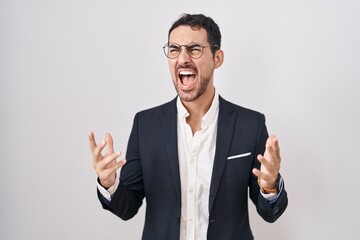 Handsome business hispanic man standing over white background crazy and mad shouting and yelling with aggressive expression and arms raised. frustration concept.
