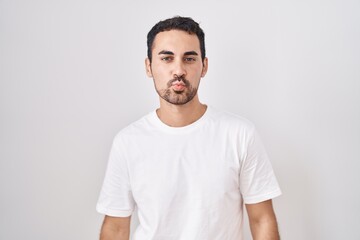 Handsome hispanic man standing over white background looking at the camera blowing a kiss on air being lovely and sexy. love expression.