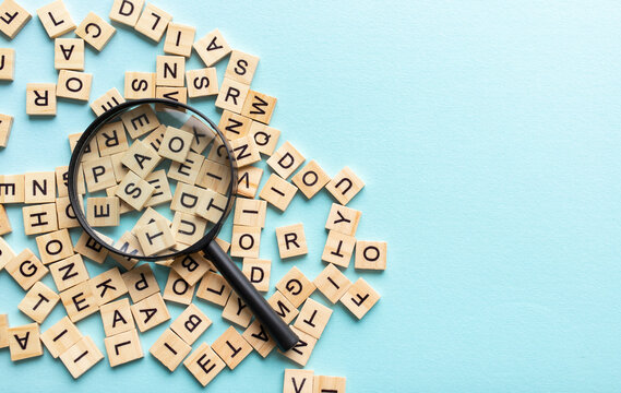 Square letter tiles with magnifying glass against blue background. Search for words and information concept