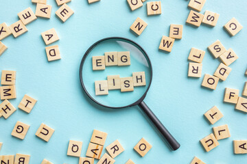 Square letter tiles with magnifying glass against blue background. Search for words and information concept