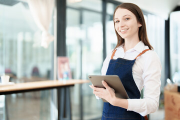 Starting and opening a small business, a young Asian woman showing a smiling face in an apron standing in front of a coffee shop bar counter. Business Owner, Restaurant, Barista, Cafe, Online SME