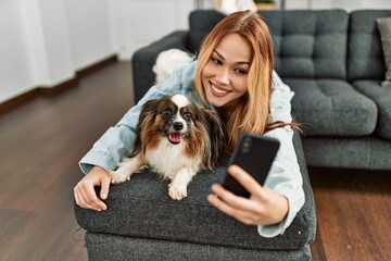 Young caucasian woman hugging dog make selfie by smartphone at home