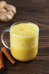 Vegan whipped turmeric golden latte from almond milk, ginger, turmeric and cinnamon in a mug, sugar and lactose free on a wooden table.