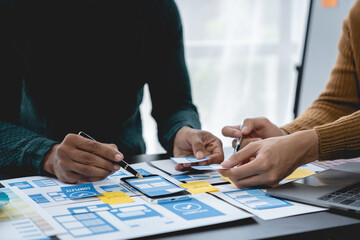 ux developers, UI designers Asian group data researchers brainstorm on tabletop mobile app interface wireframe design client summary color codes modern office Creative Digital Development Agency.
