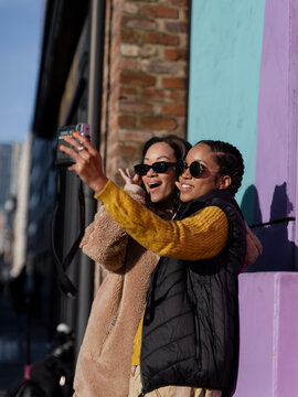 Two young women taking selfies by colorful graffiti wall