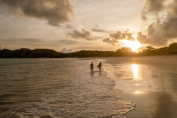 Indonesia, Lombok, Silhouette of surfers walking on beach at sunset