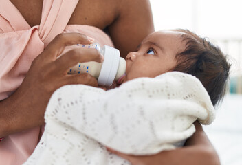 African american baby sucking feeding bottle at bedroom