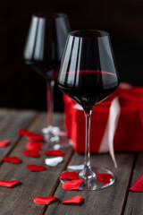 Saint Valentine's Day celebration. Wineglasses with red wine, hearts, gift box, postcard on dark wooden background. Happy holiday . Table decor for festive dinner, romantic atmosphere